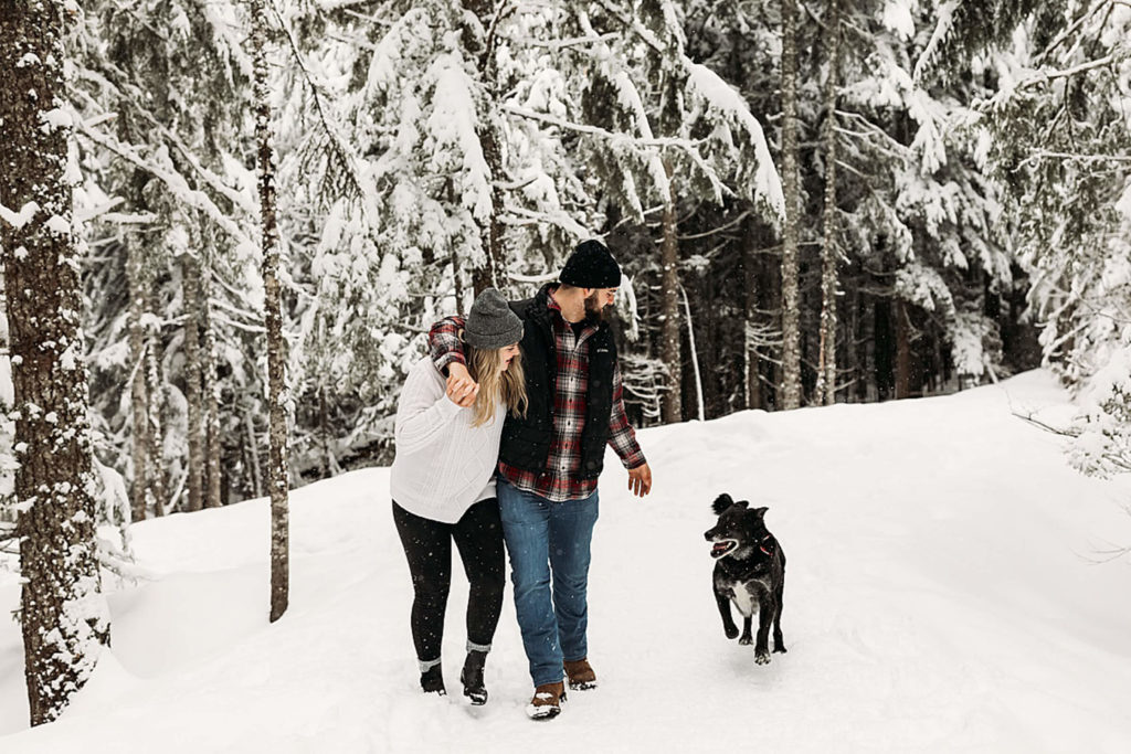 man and woman walking in the snow with their old dog running beside them