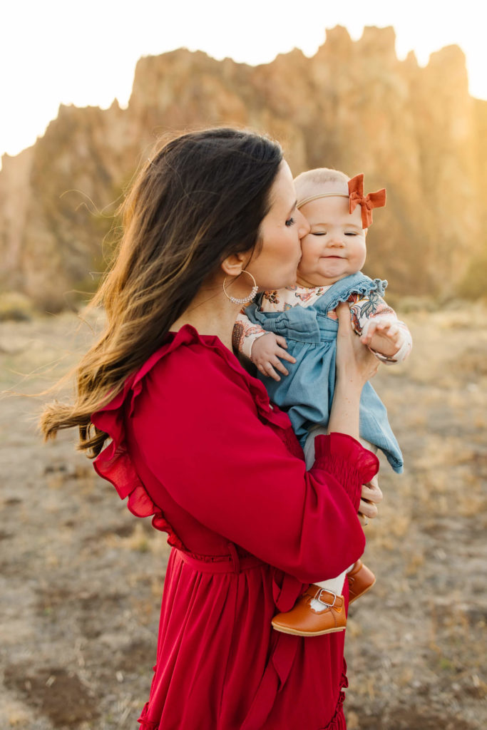 brunette in red kissing baby in front of smith rock 