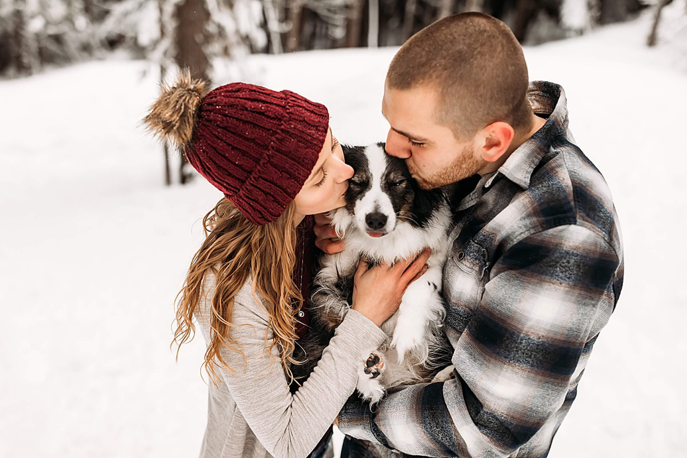 male and female in the snow kissing their puppy