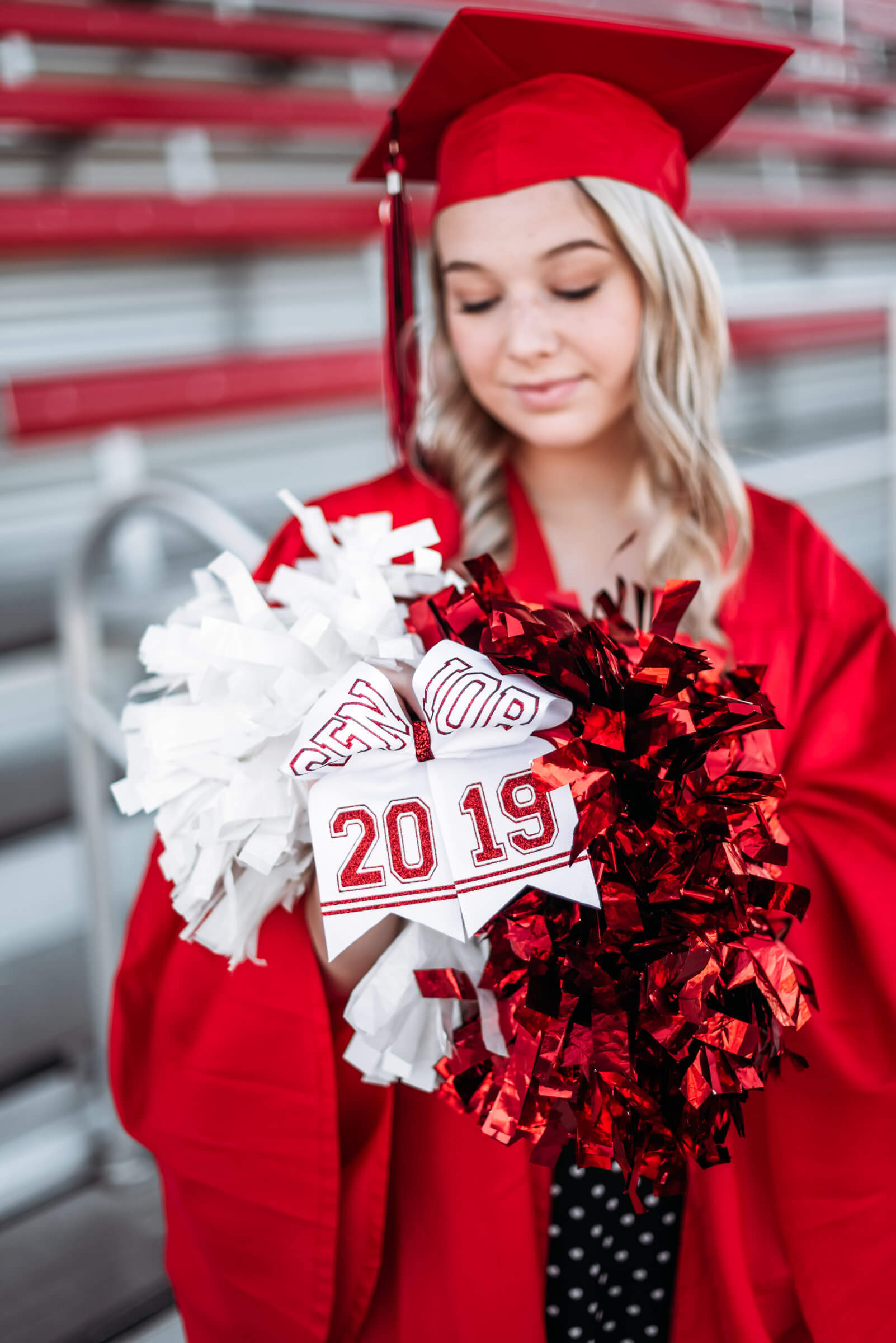 blonde girl with red graduation cap and gown on looking at cheer pom poms
