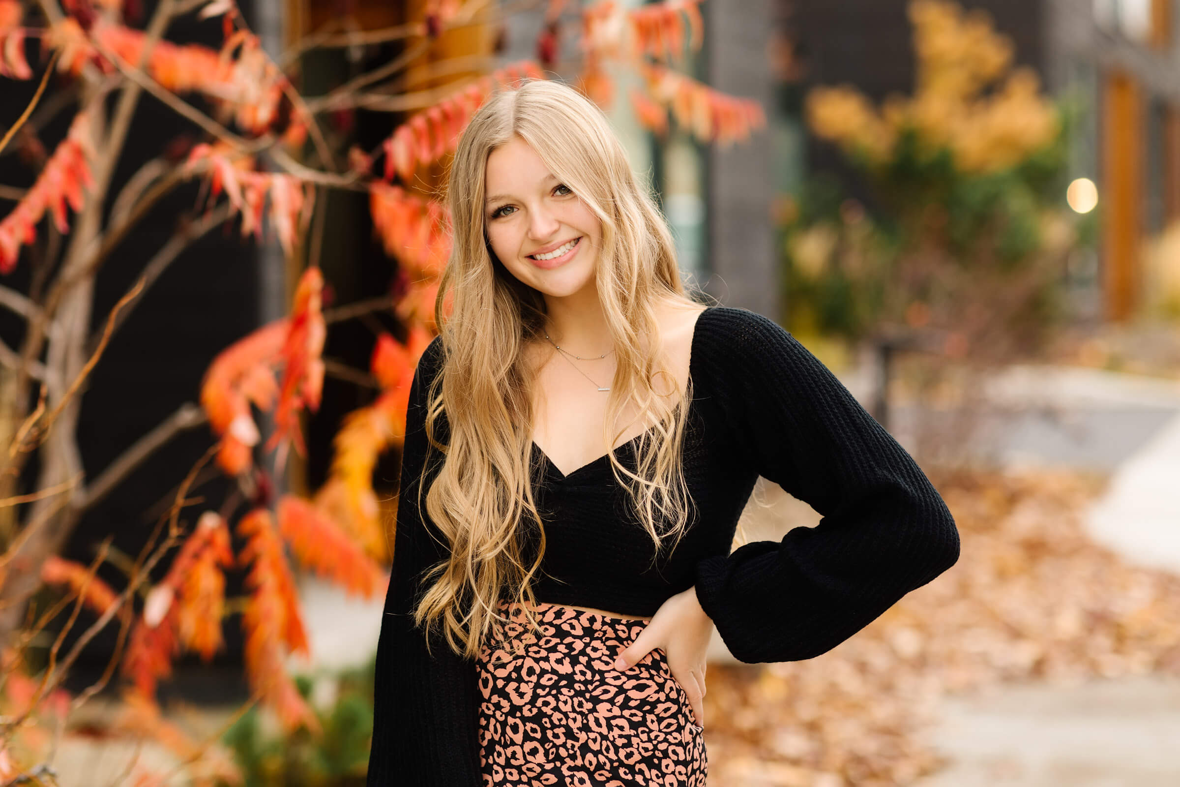 blonde senior girl in black top standing in front of orange trees in bend