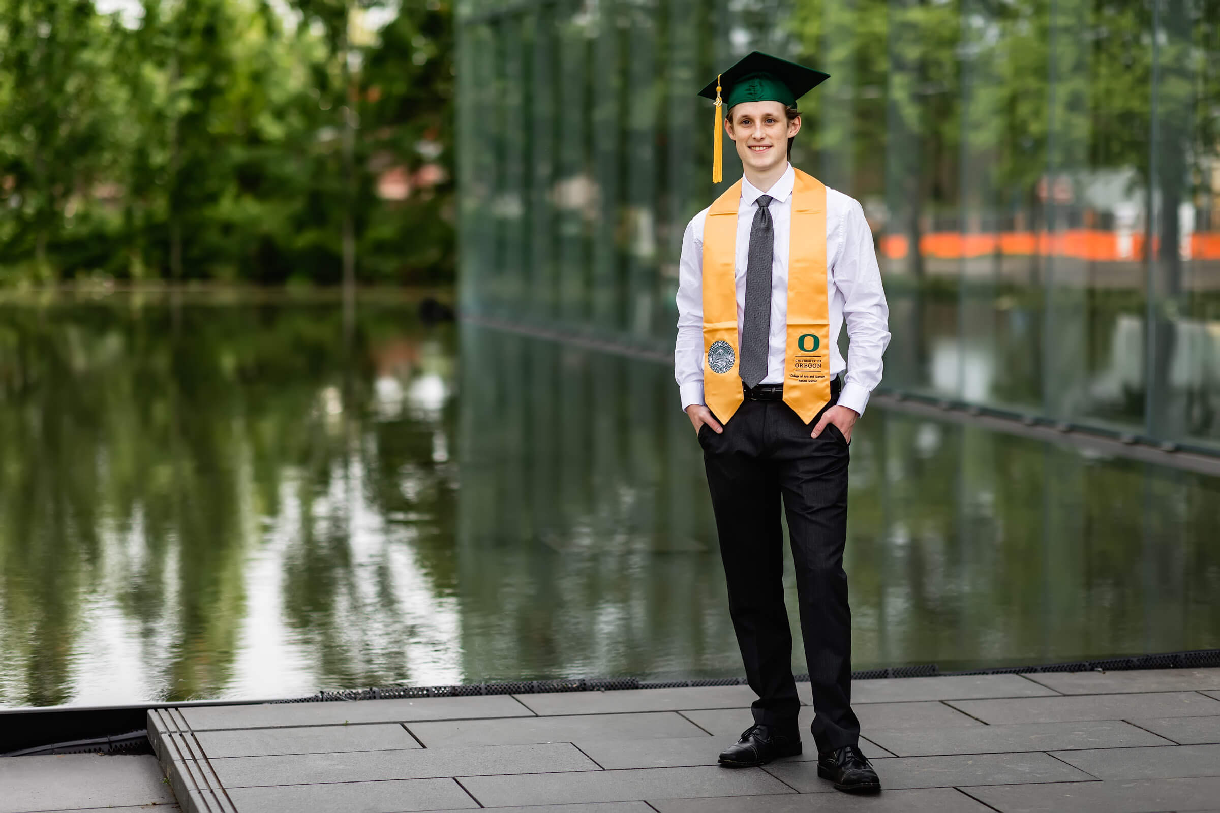 Male wearing university of Oregon graduation cap in front of John E. Jaqua Center for Student Athletes