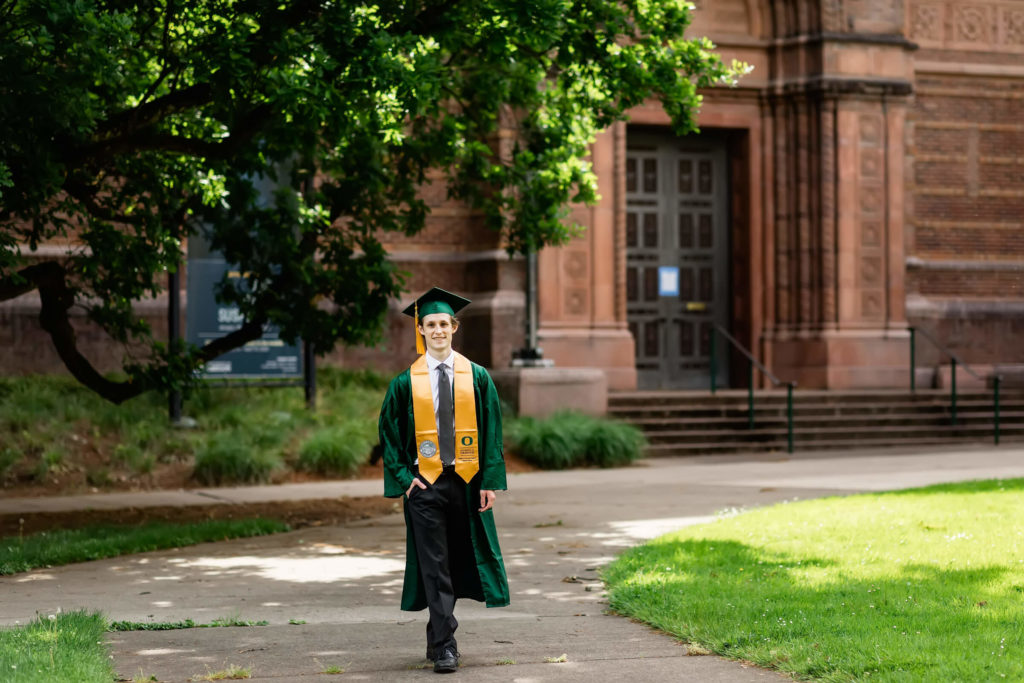 male walking through university of Oregon memorial quad in green graduation cap and gown