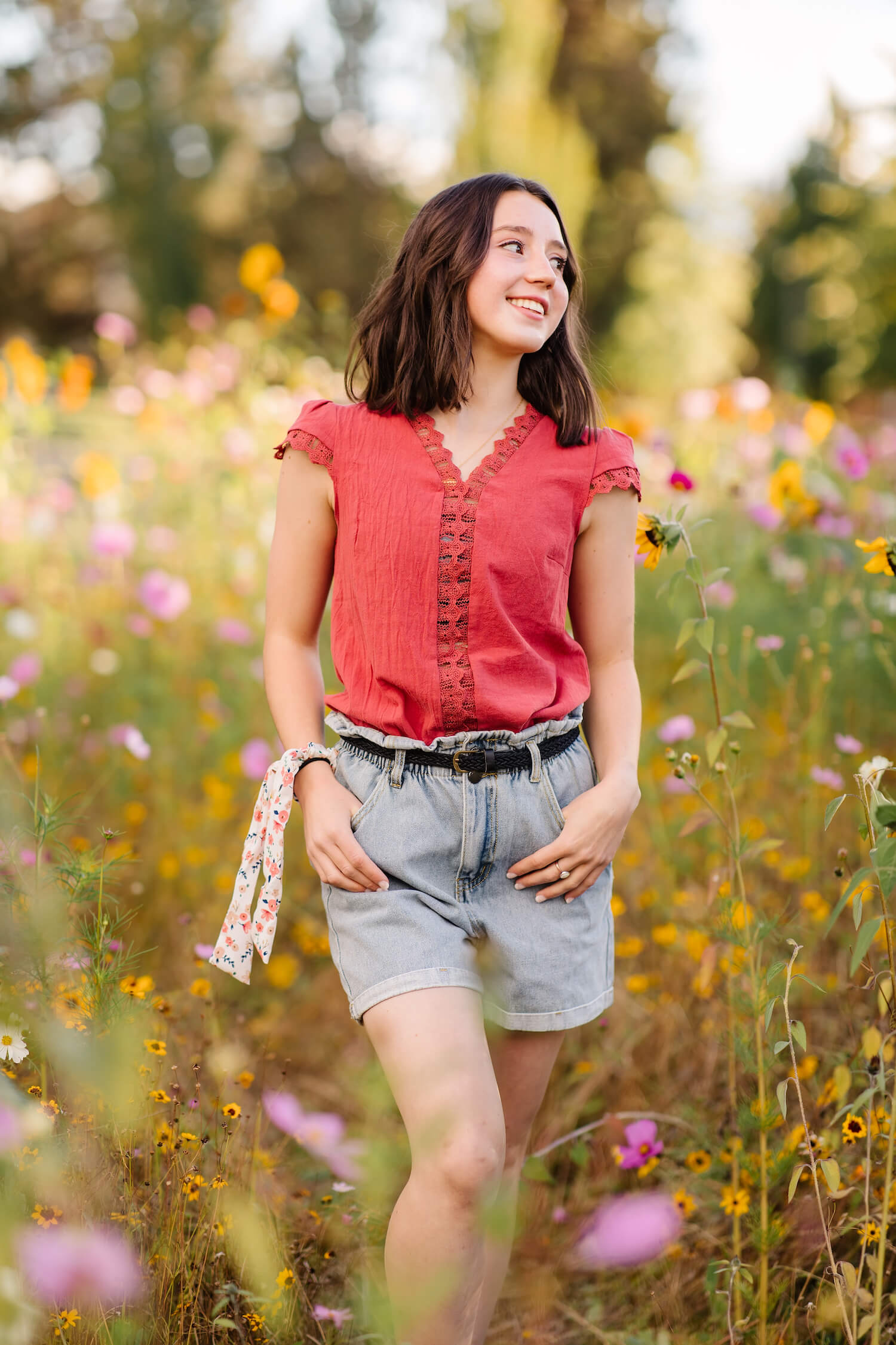 brunette in pink shirt and denim shorts standing in wild flower field