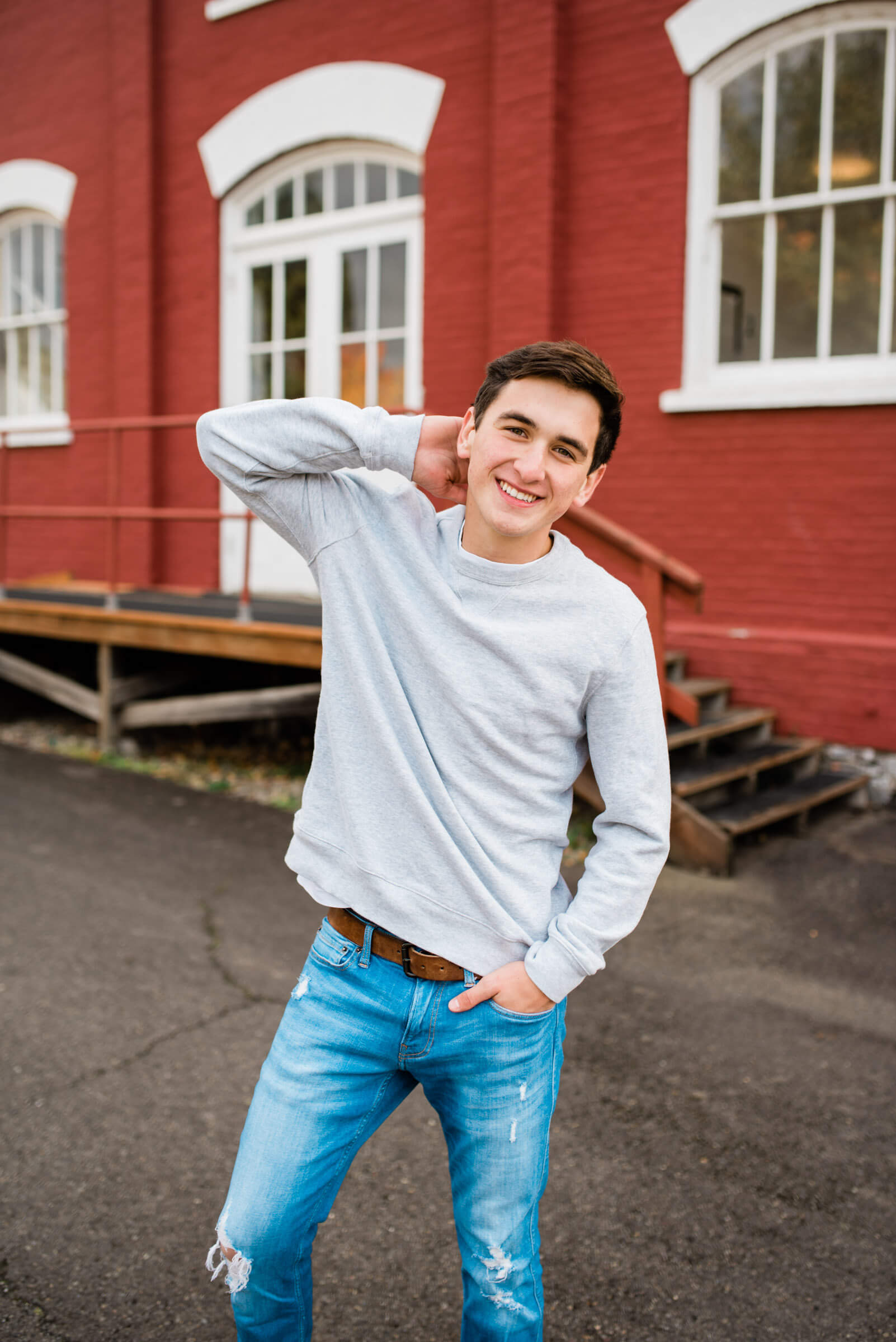 senior boy walking away from red building and rubbing neck during senior portraits