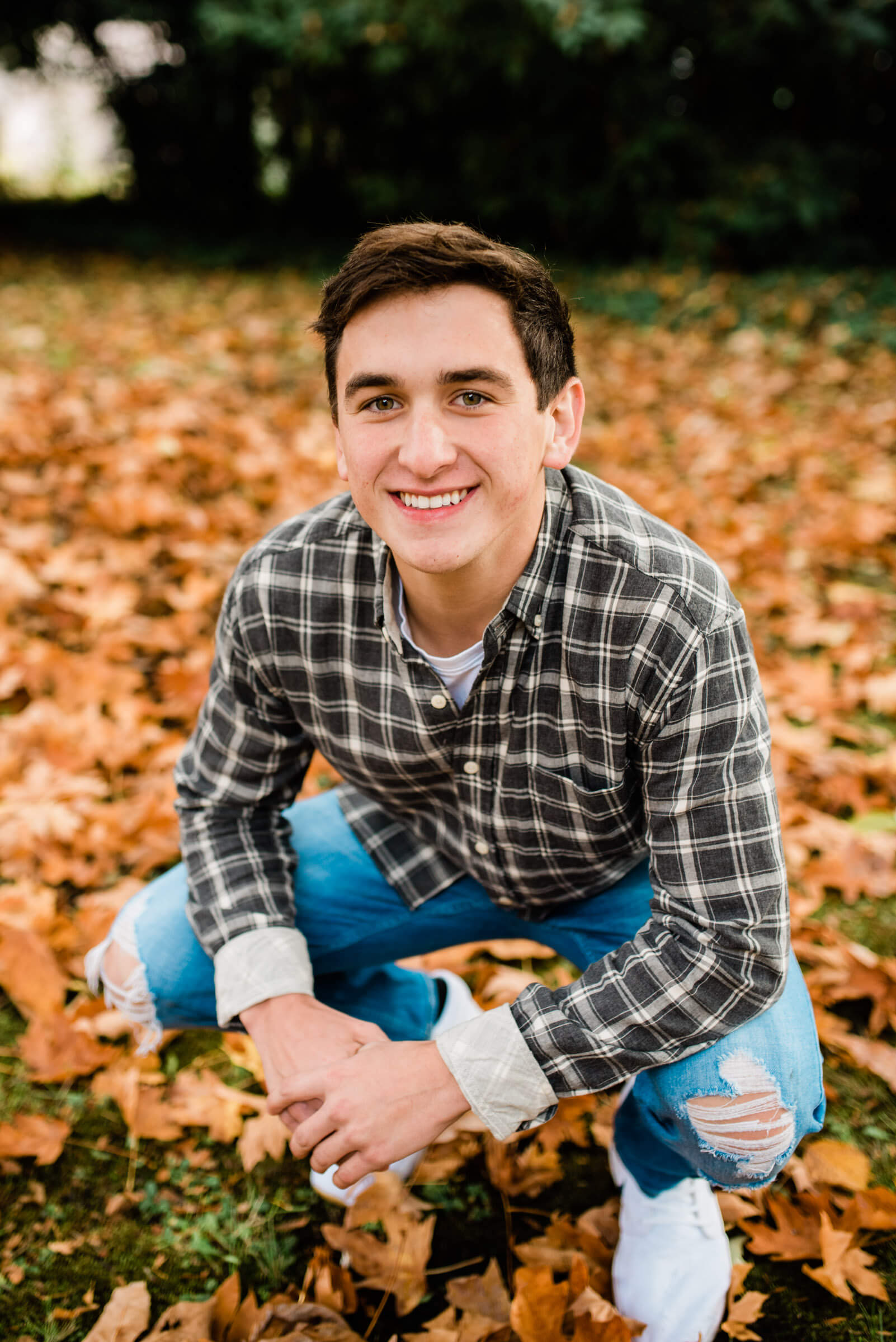 senior boy kneeling around fall leaves during senior portraits