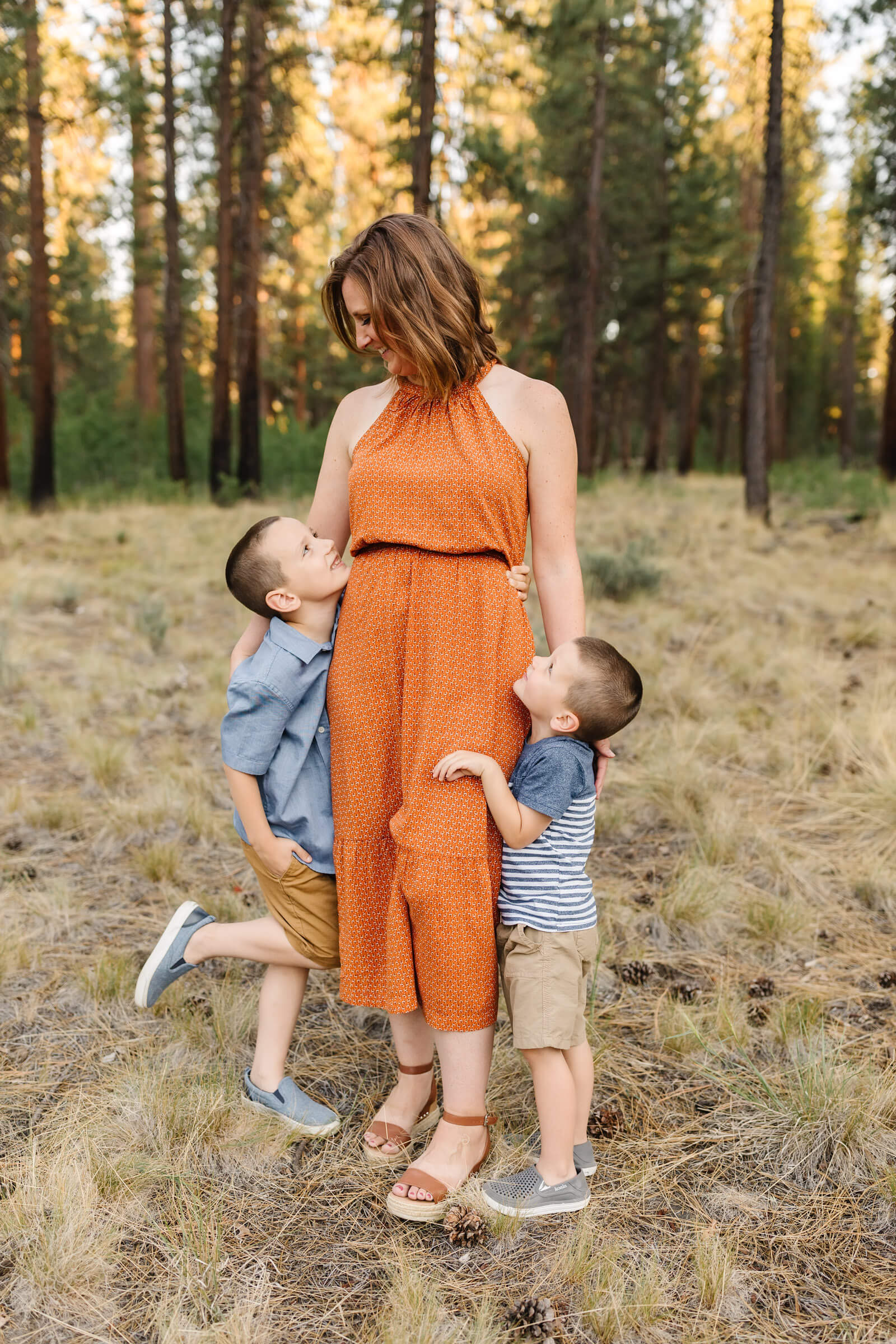 woman in orange dress with two boys hugging her legs