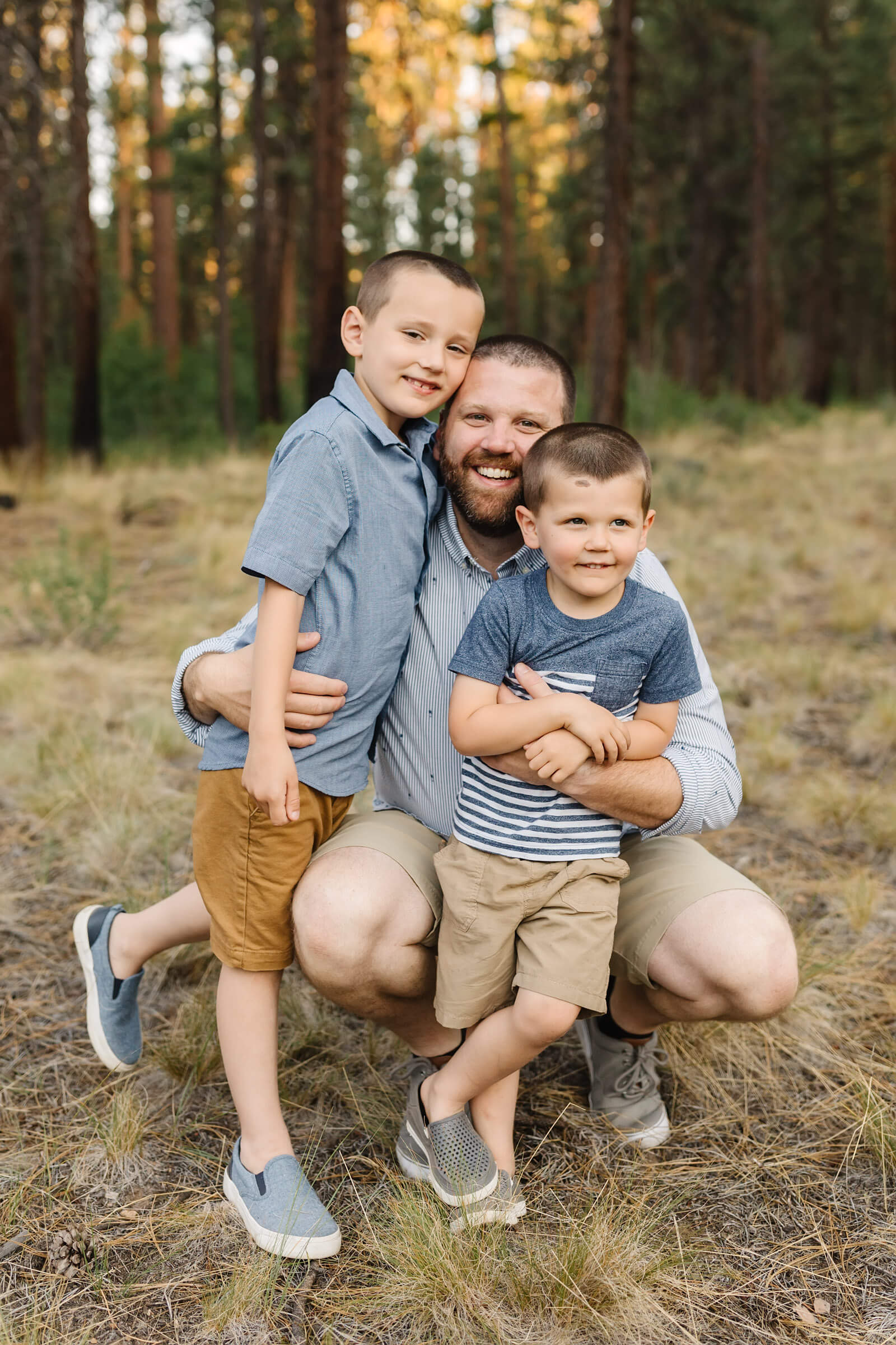 dad kneeling down to hug his two boys during family session