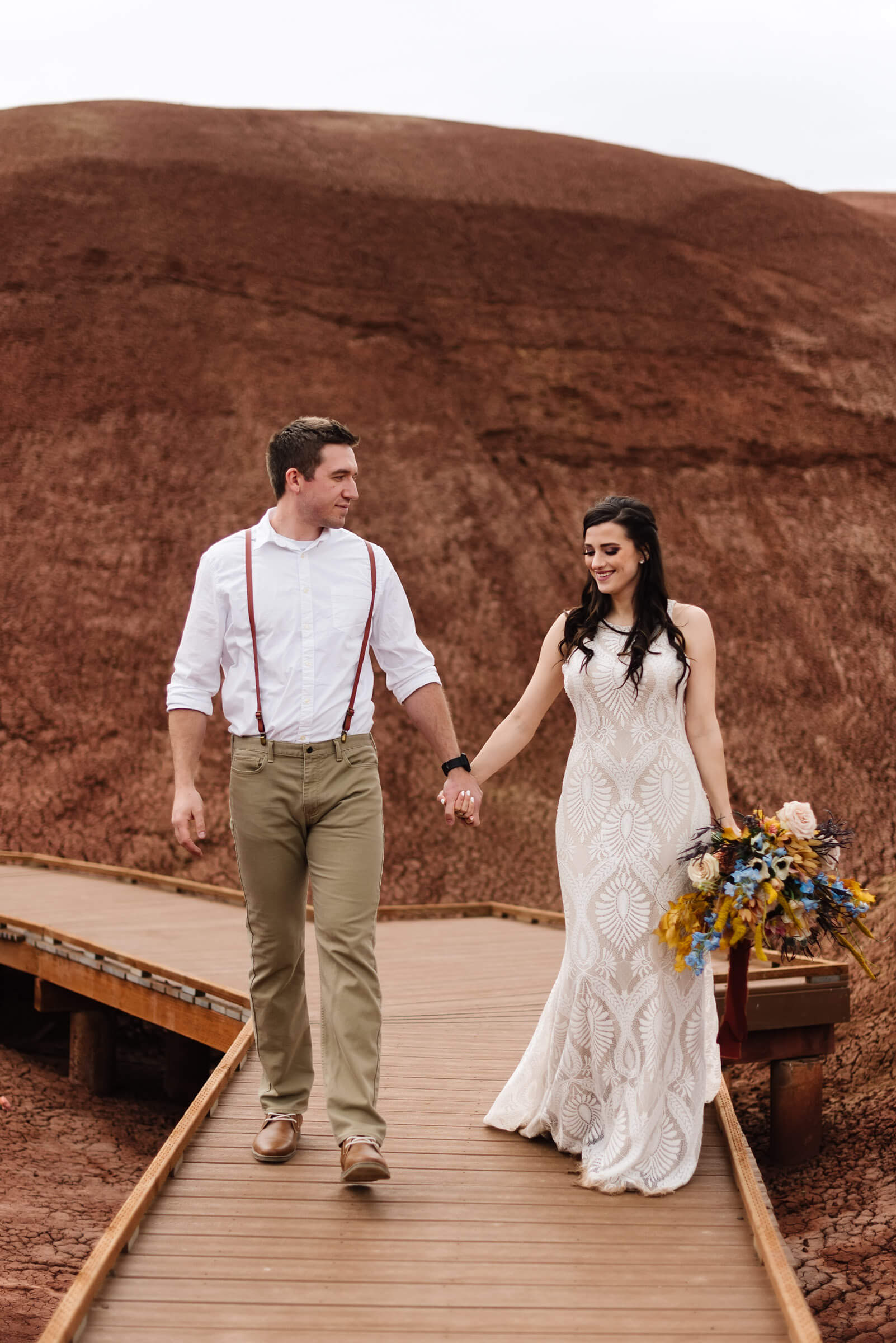 bride and groom holding hands walking through painted hills during wedding portraits