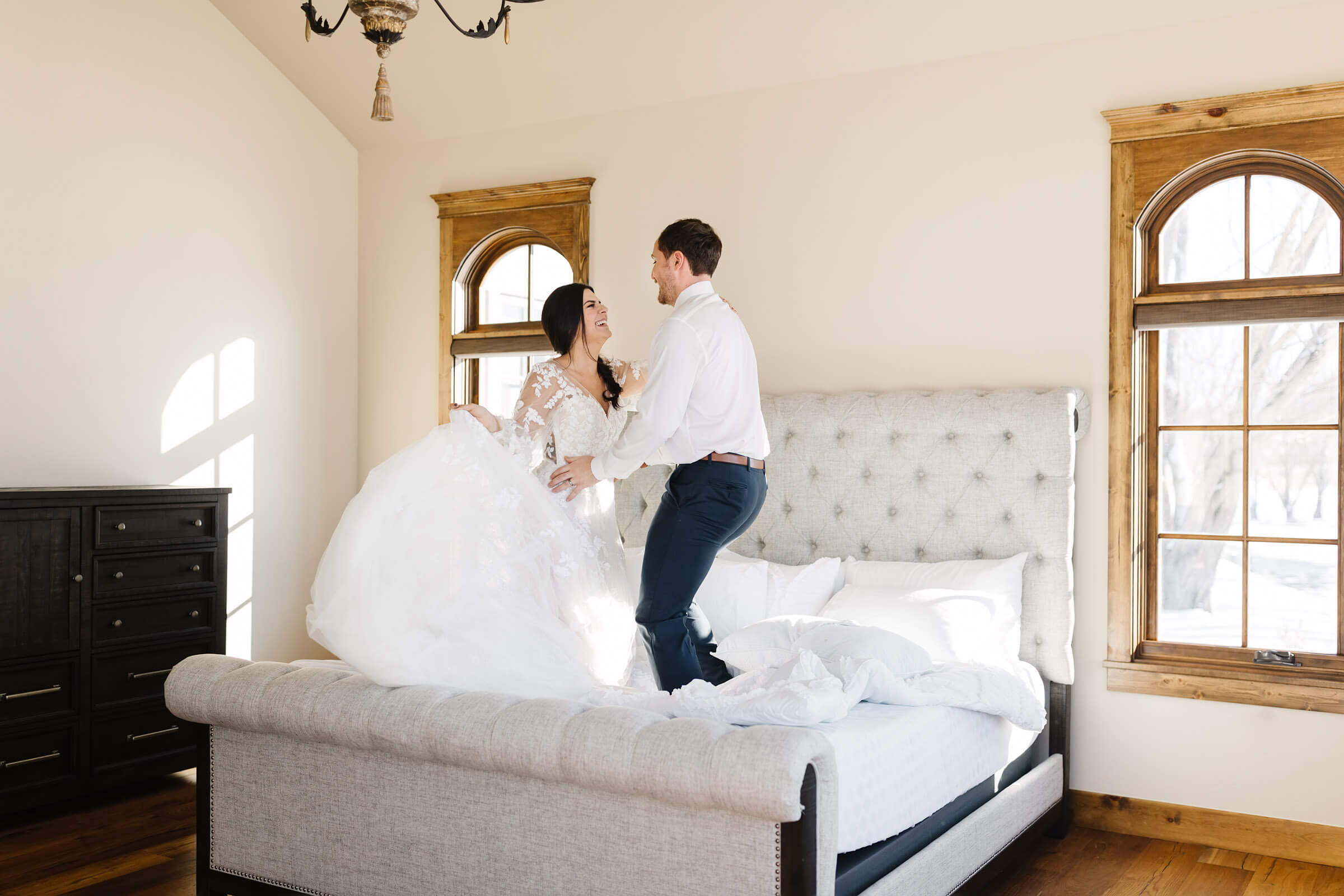 bride and groom jumping on bed in bridal attire