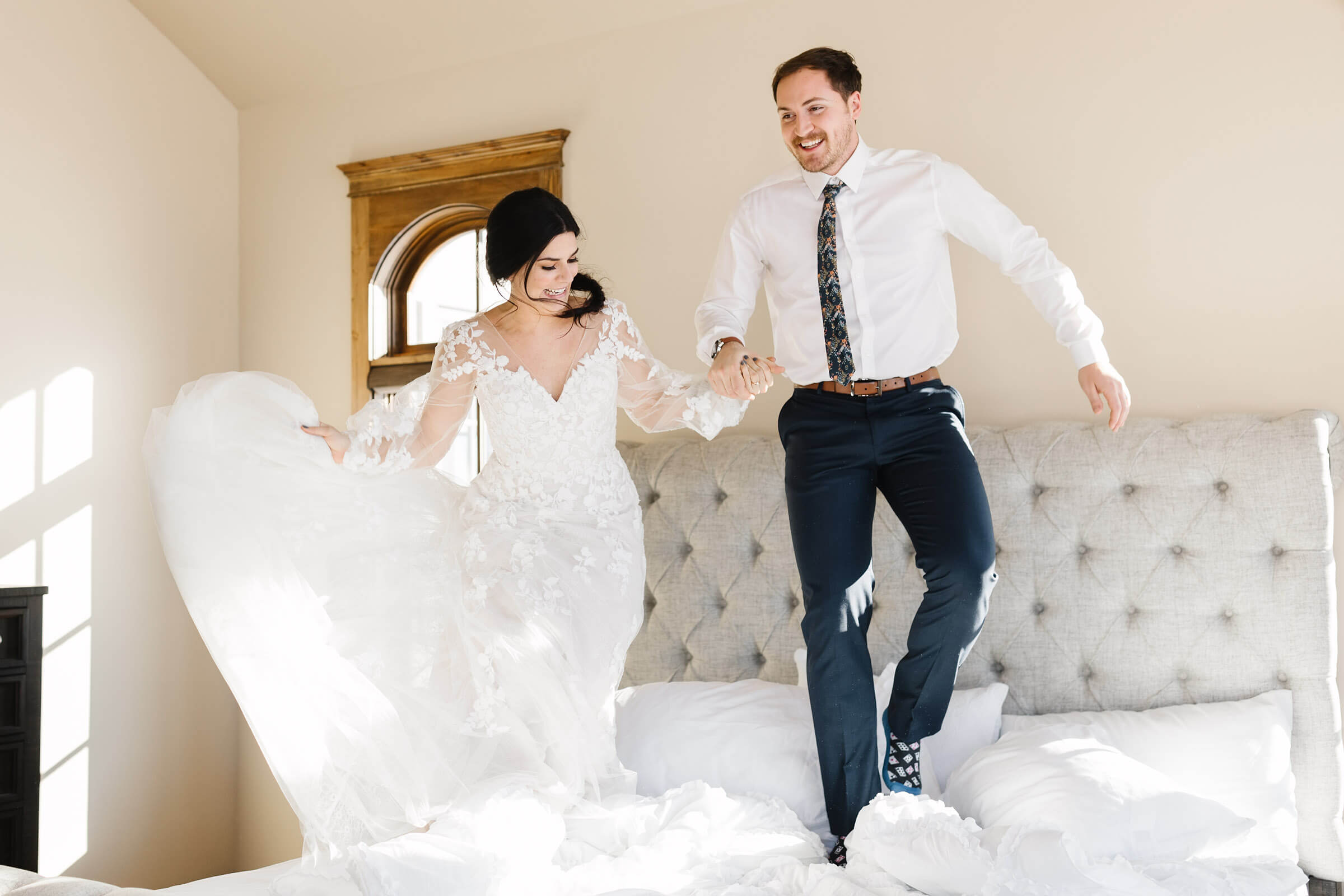 bride and groom holding hands jumping on bed