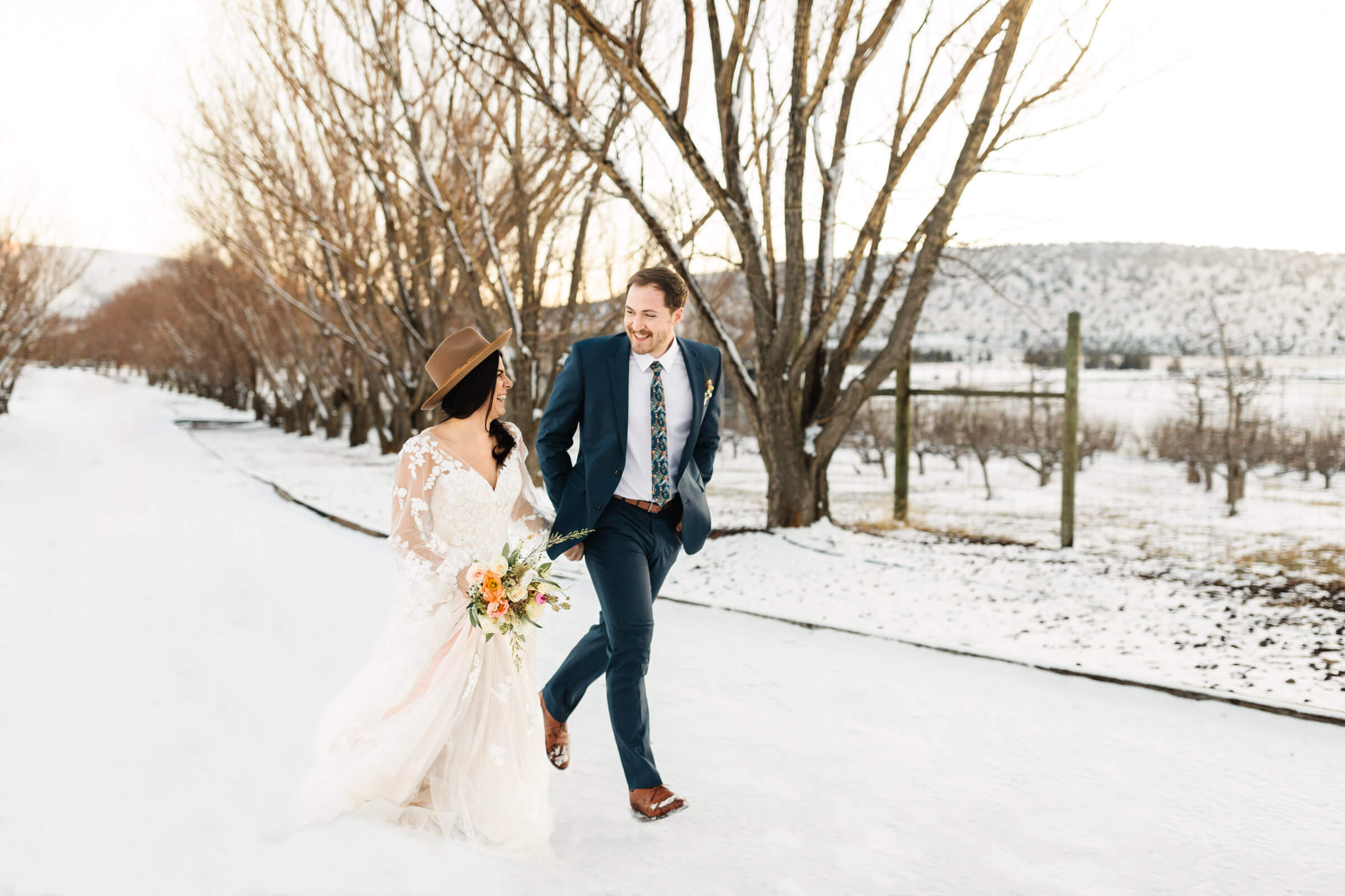 bride and groom holding hands running in snow