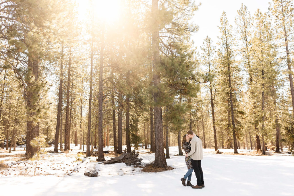 man and woman hugging and kissing in snow with sun rise behind them