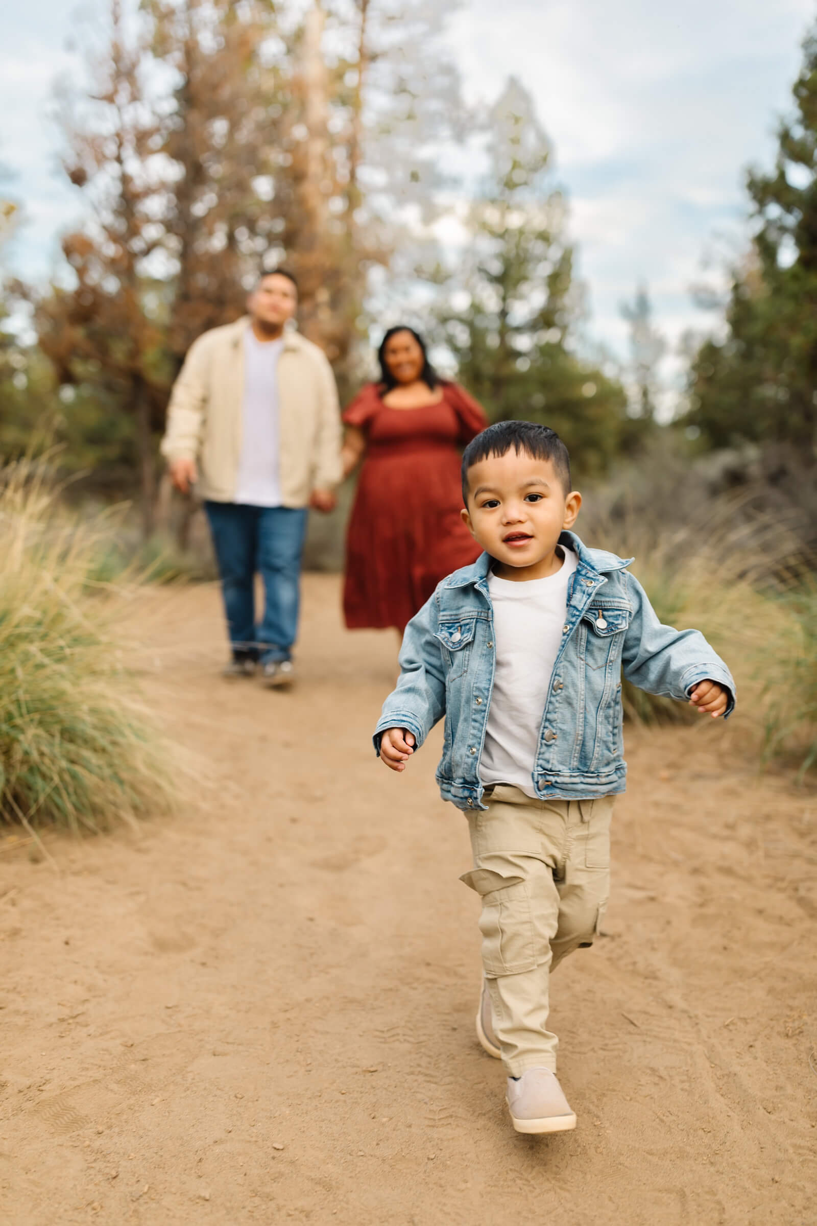 little boy in denim jacket running in front of mom and dad