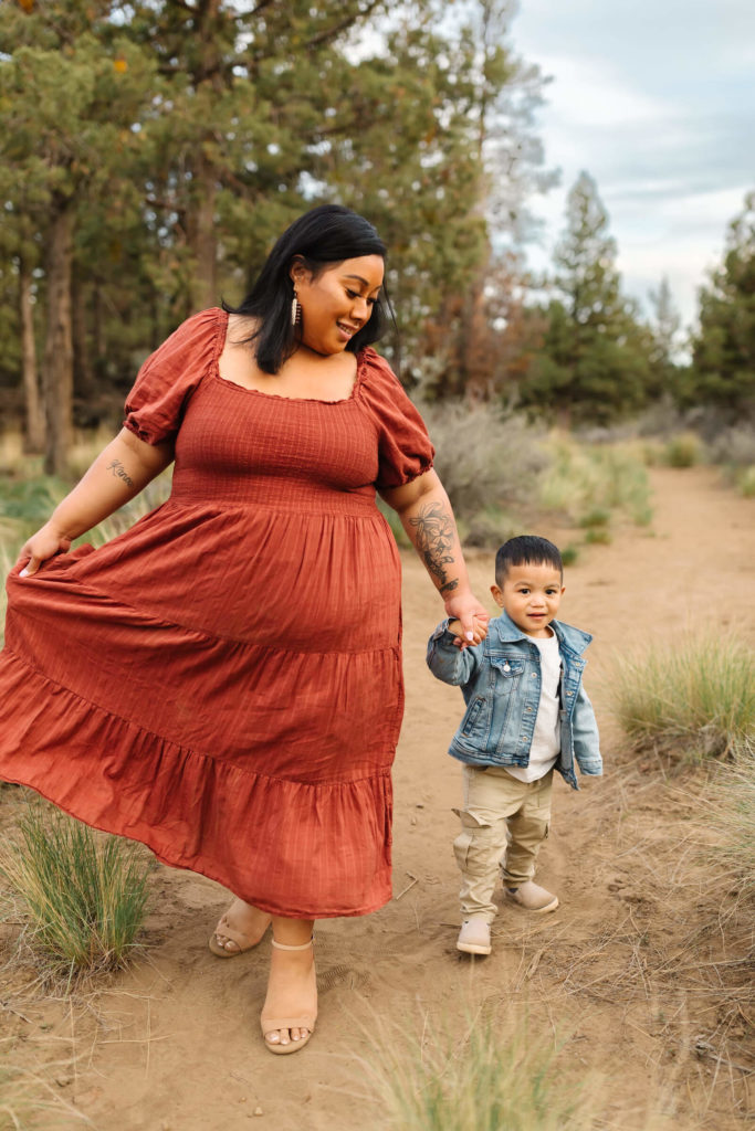 woman with black hair and red dress holding hands with little boy in blue denim jacket