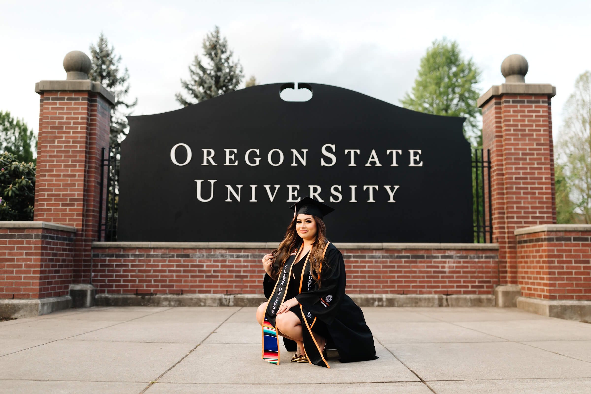 girl in black graduation cap and gown in front of Oregon State University Sign