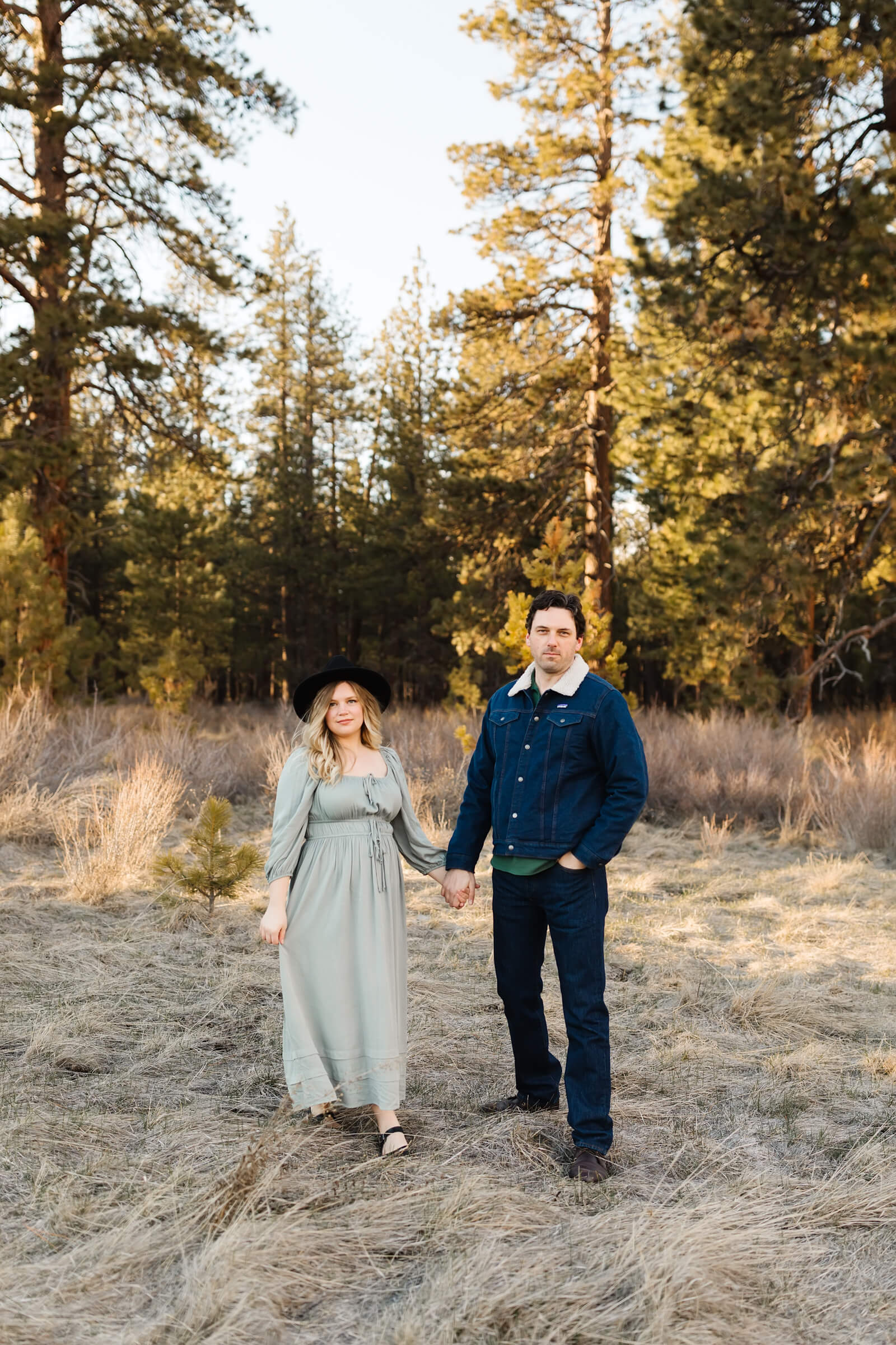blonde girl in green dress holding hands with man in denmin coat in open field at Dillon falls Bend Oregon
