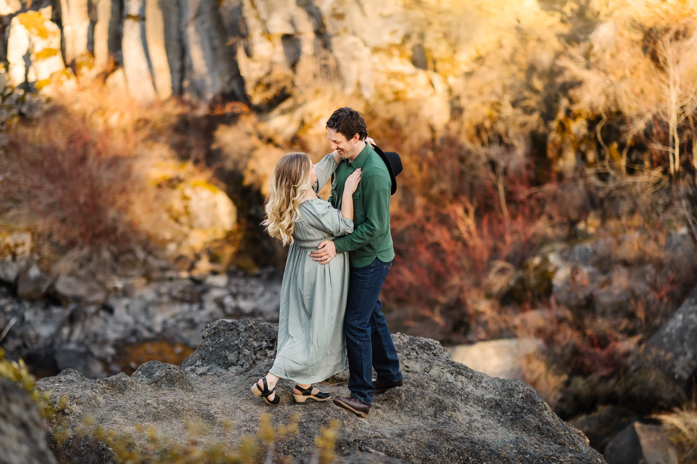 blonde girl in green dress holding man in green shirt on cliffs above Dillon falls Bend Oregon
