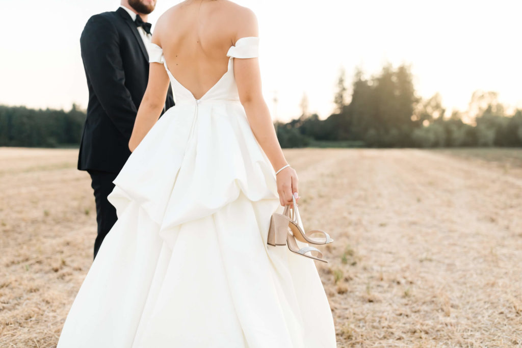 bride in white wedding dress holding tan heels with groom in black tuxedo