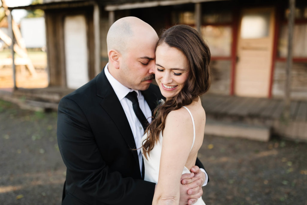 man in black suit kissing bride in white wedding dress on cheek