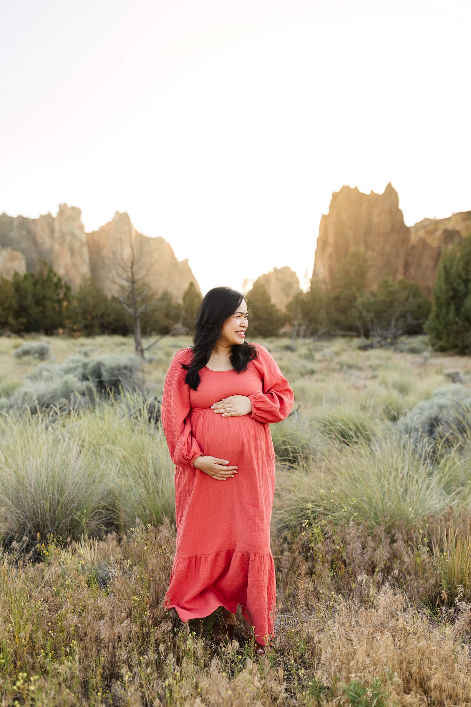 woman in coral dress holding pregnant belly during smith rock maternity photoshoot