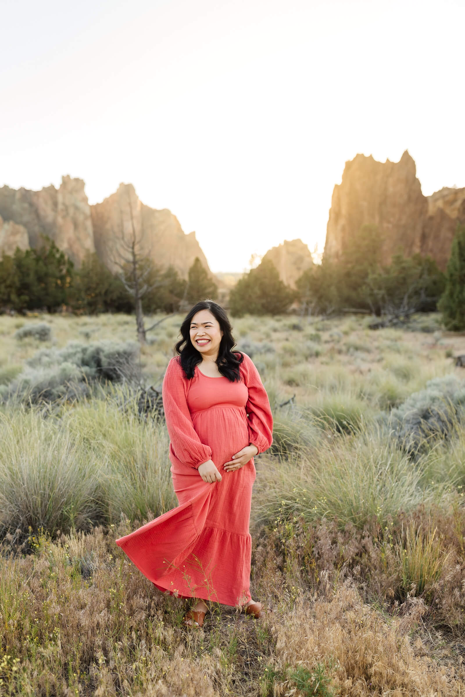 woman wearing coral dress holding pregnant belly during smith rock maternity photoshoot