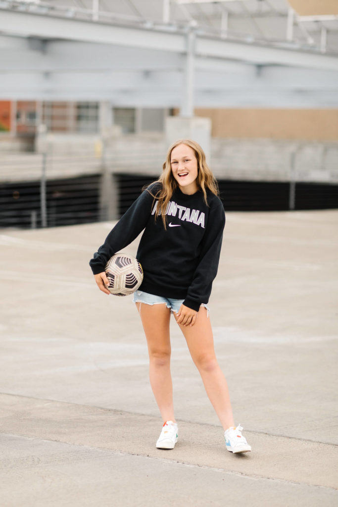 blonde girl in black Montana sweatshirt with soccer ball in downtown bend