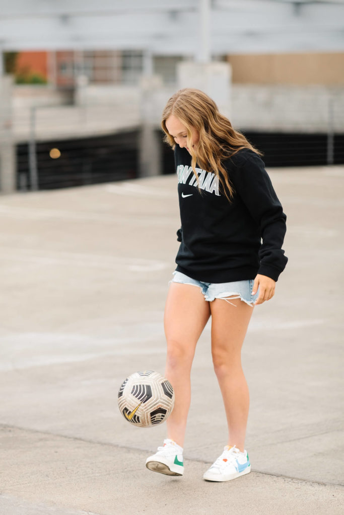 blonde girl in black Montana sweatshirt juggling soccer ball in downtown bend