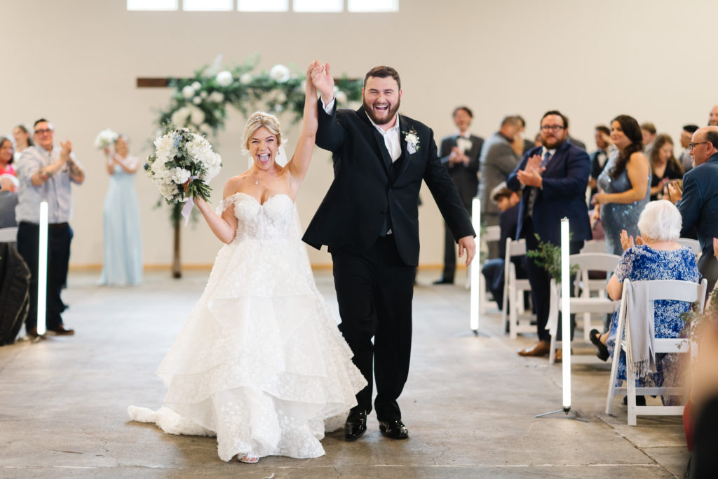 bride and groom cheering as they walk up aisle in barn wedding