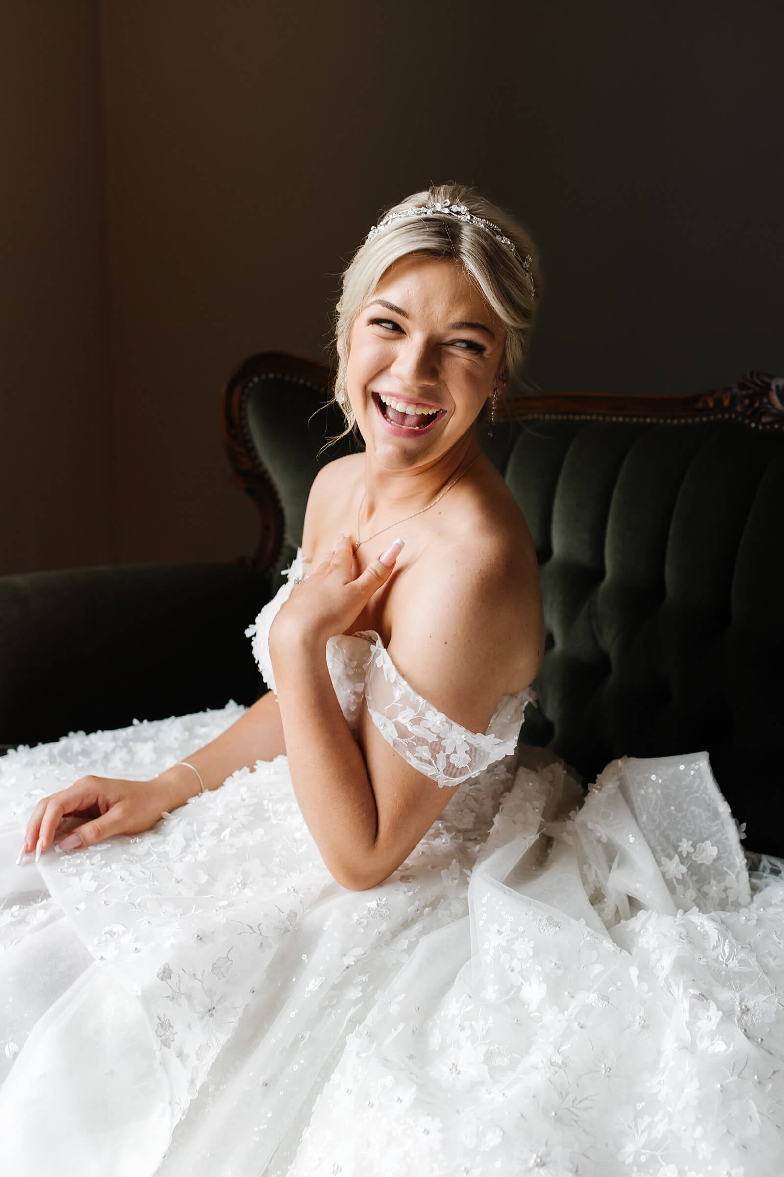 blonde bride sitting on green velvet couch laughing
