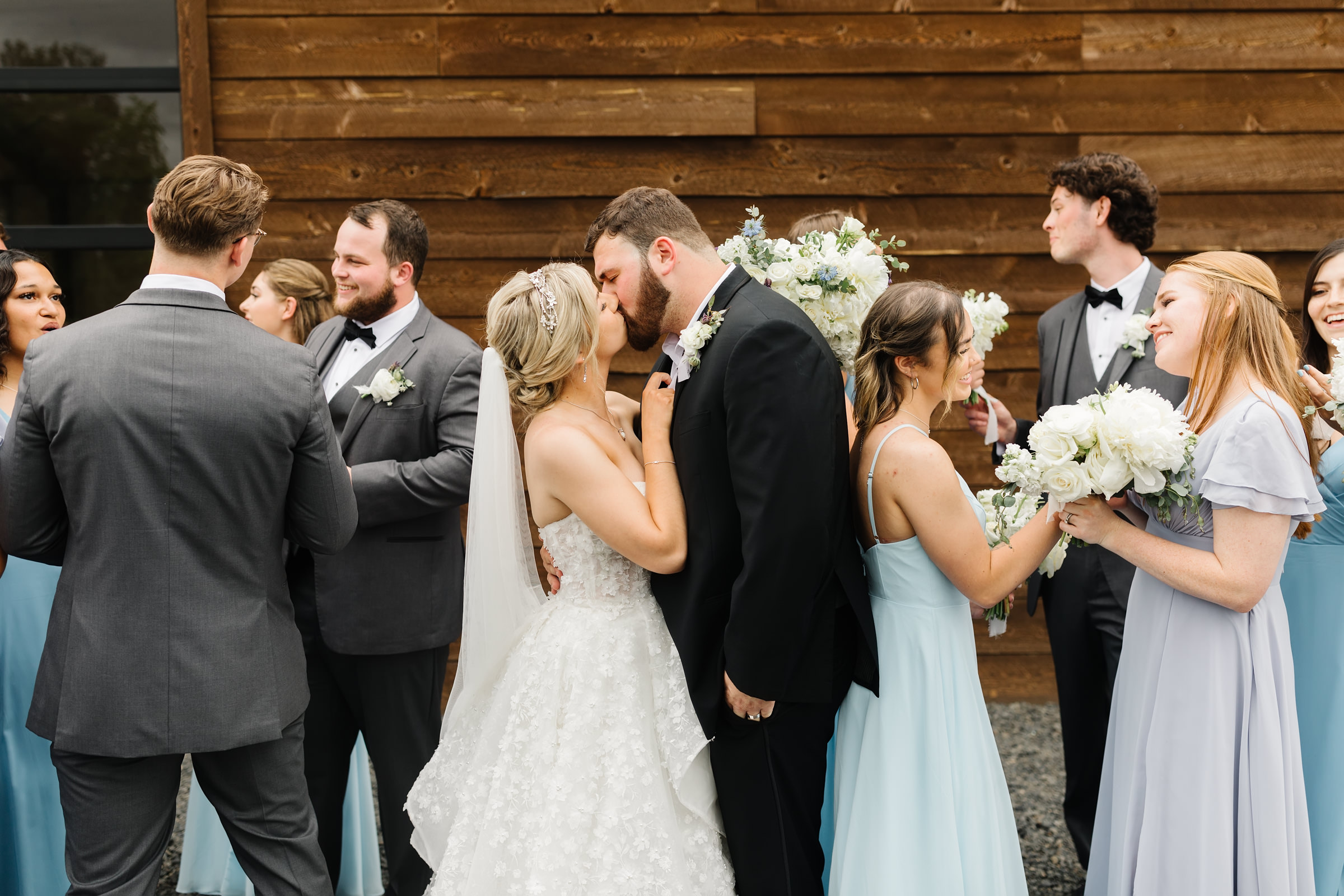 bride and groom kissing while their bridal party talks