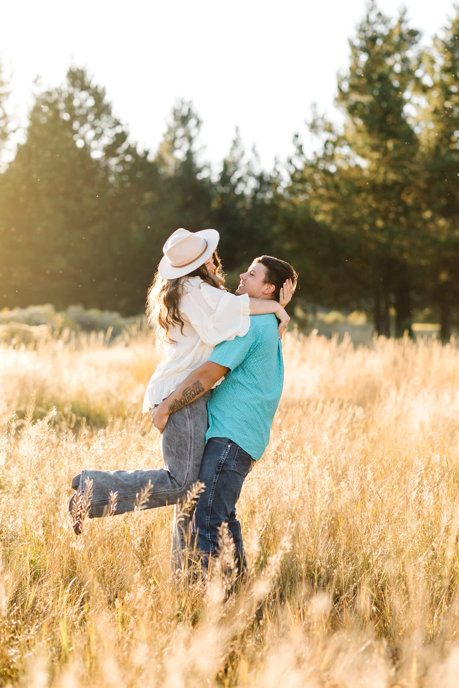 brunette male in teal button up lifting girl while in golden hay field as she looks at him