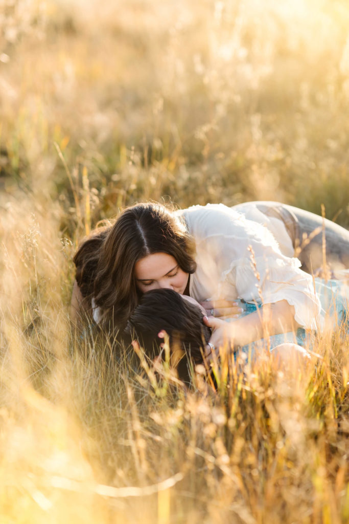 brunette girl in white laying with man in teal button up in golden hay field