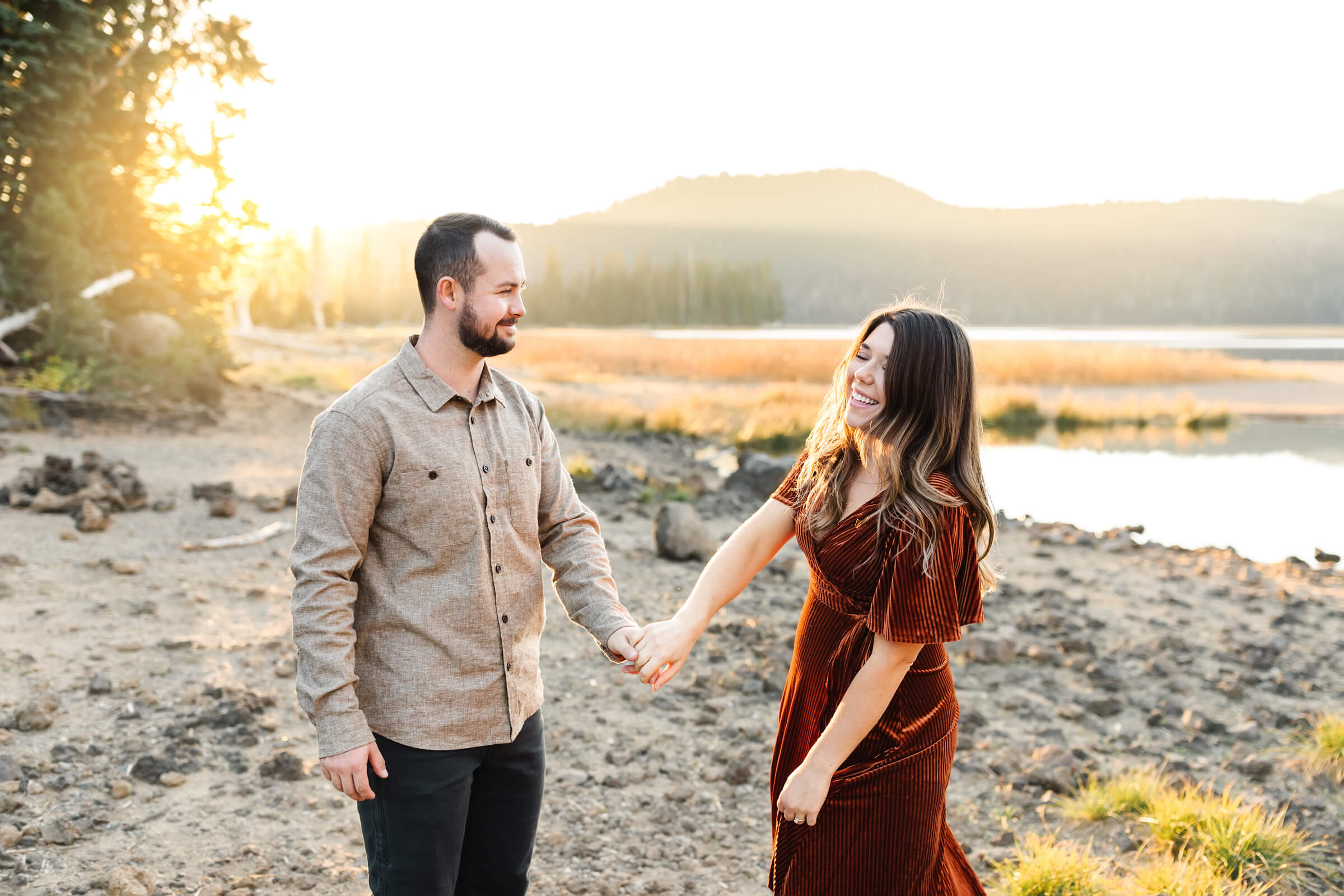 girl in orange velvet dress holding mans hand during engagement photos at sparks lake