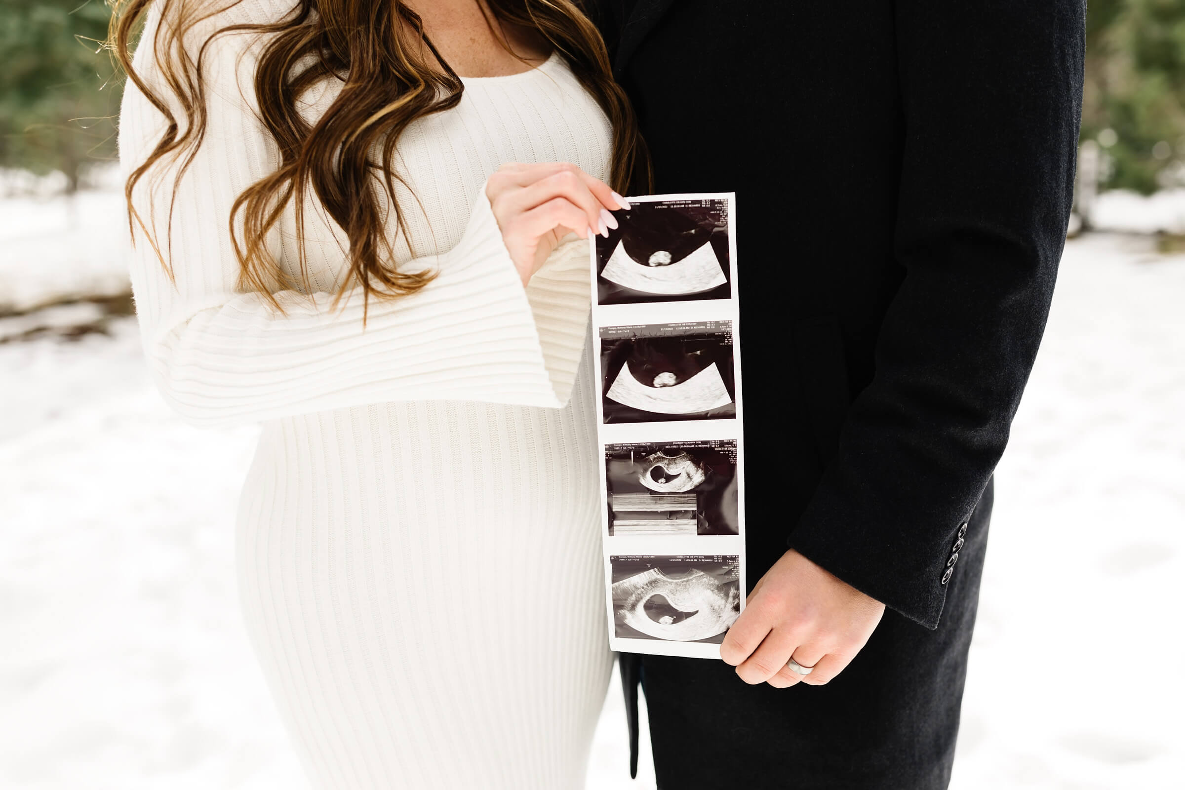 woman in white knit dress and man holding sonogram for pregnancy announcement