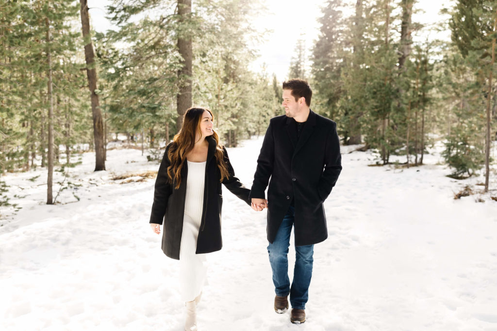 man and woman walking holding hands in snow during pregnancy announcement shoot
