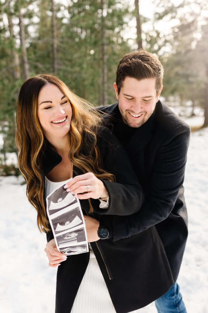 woman holding sonogram and being hugged from behind by her husband during pregnancy announcement shoot
