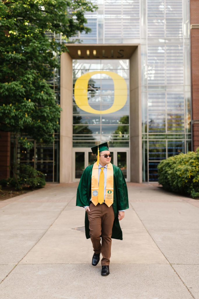 male student in university of Oregon green graduation gown outside Lillis business complex looking in the distance during Hayward field graduation photos