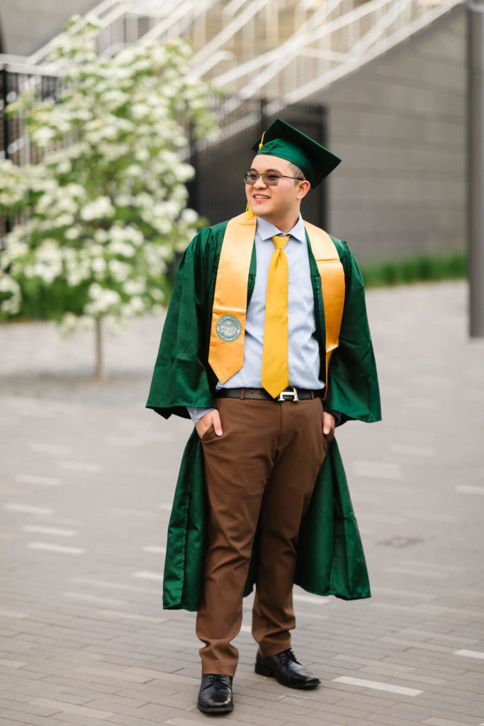 Male university of oregon student in green graduation gown standing outside of Hayward field for graduation photos