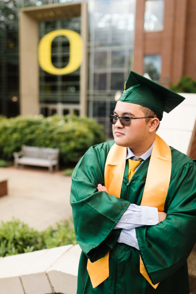 male student in university of Oregon green graduation gown outside Lillis business complex looking away from camera during Hayward field graduation photos