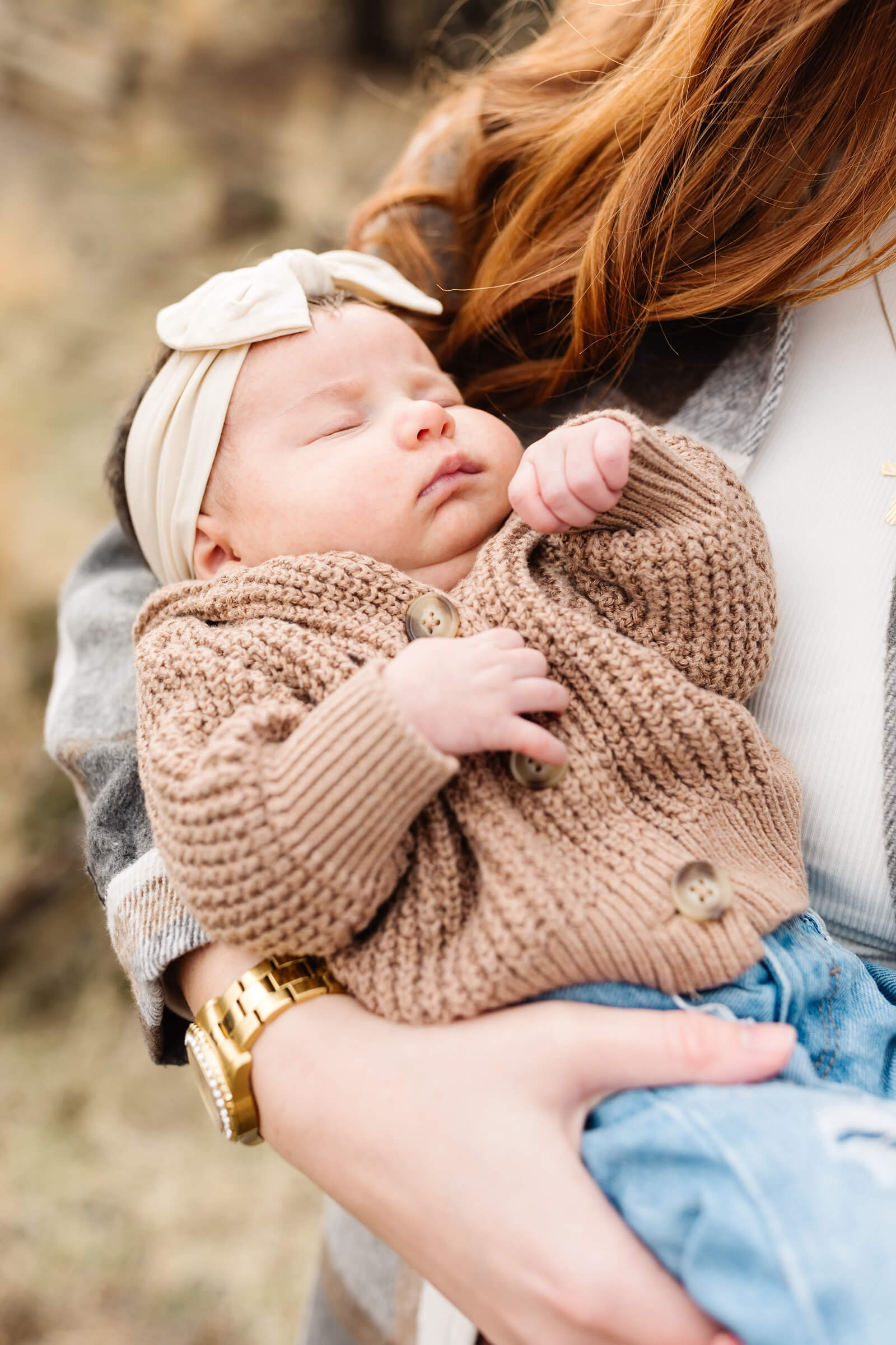 newborn baby with dark hair and cream colored headband with large bow being held during smith rock family photoshoot