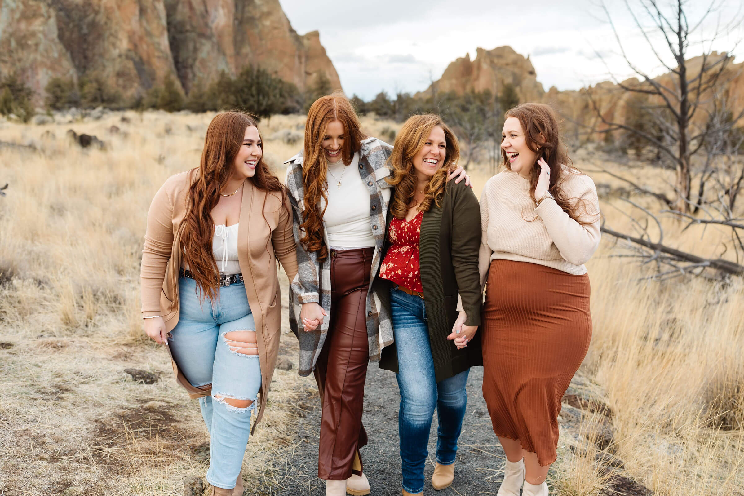 four women with red hair holding hands and walking together laughing during smith rock family photoshoot