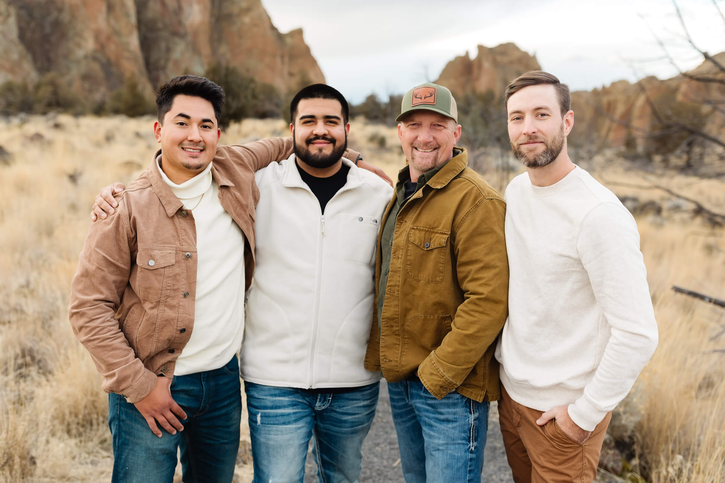 four men in tan, blue and white colors standing in front of smith rock during family photoshoot