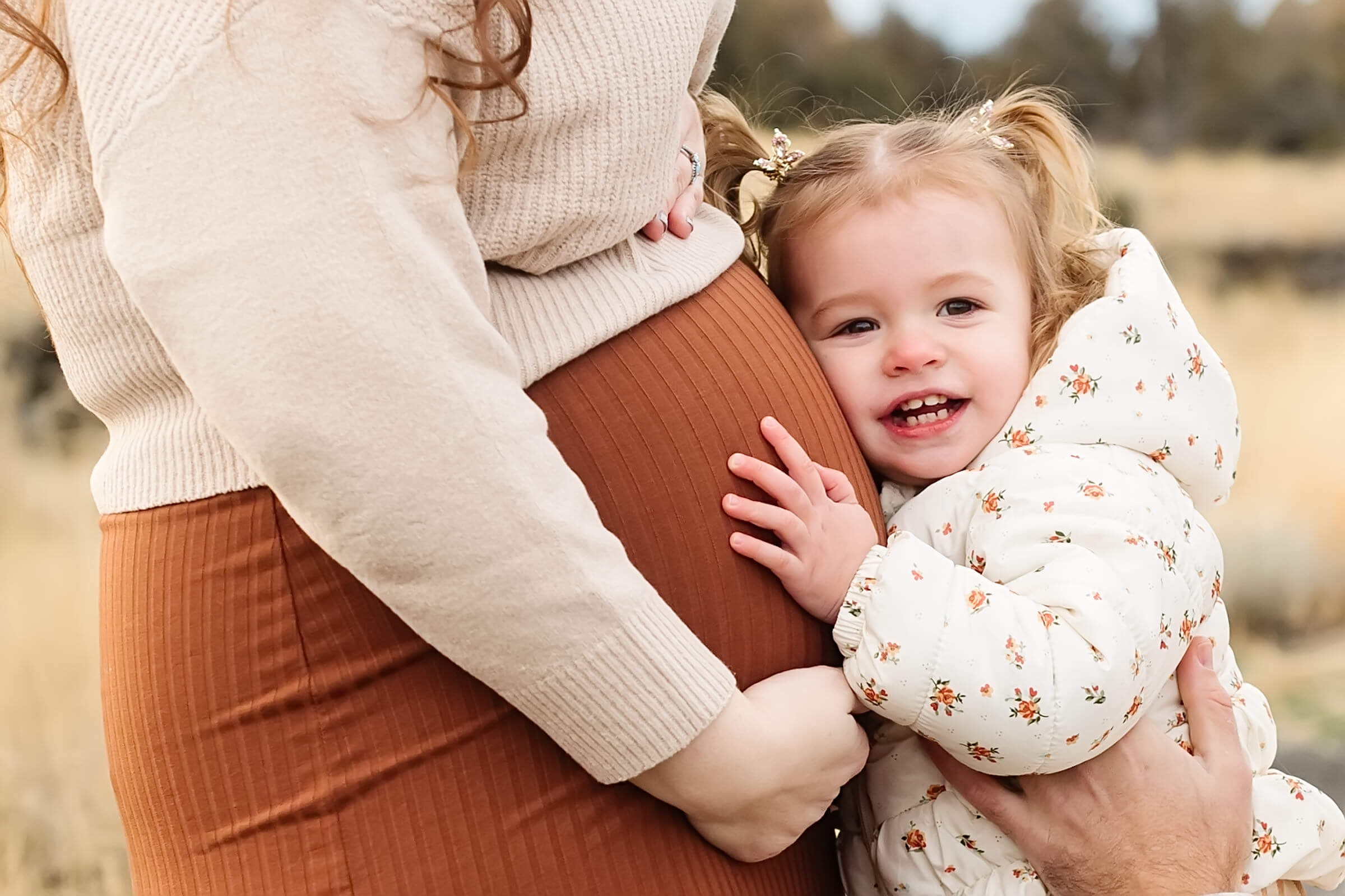 little girl with pigtails listening to mothers pregnant belly during smith rock family photoshoot