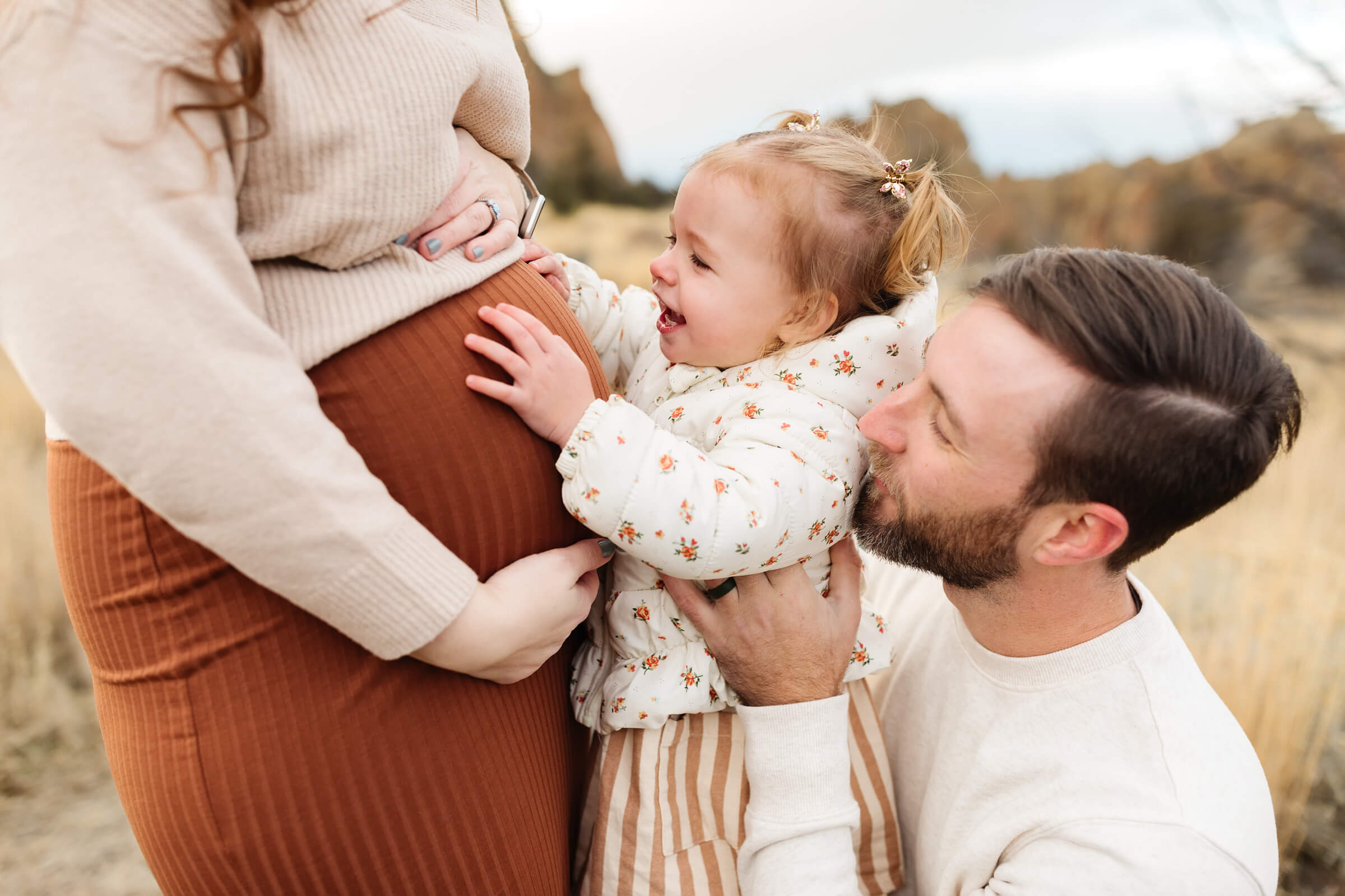 little girl with pigtails touching mothers pregnant belly during family photoshoot in central oregon