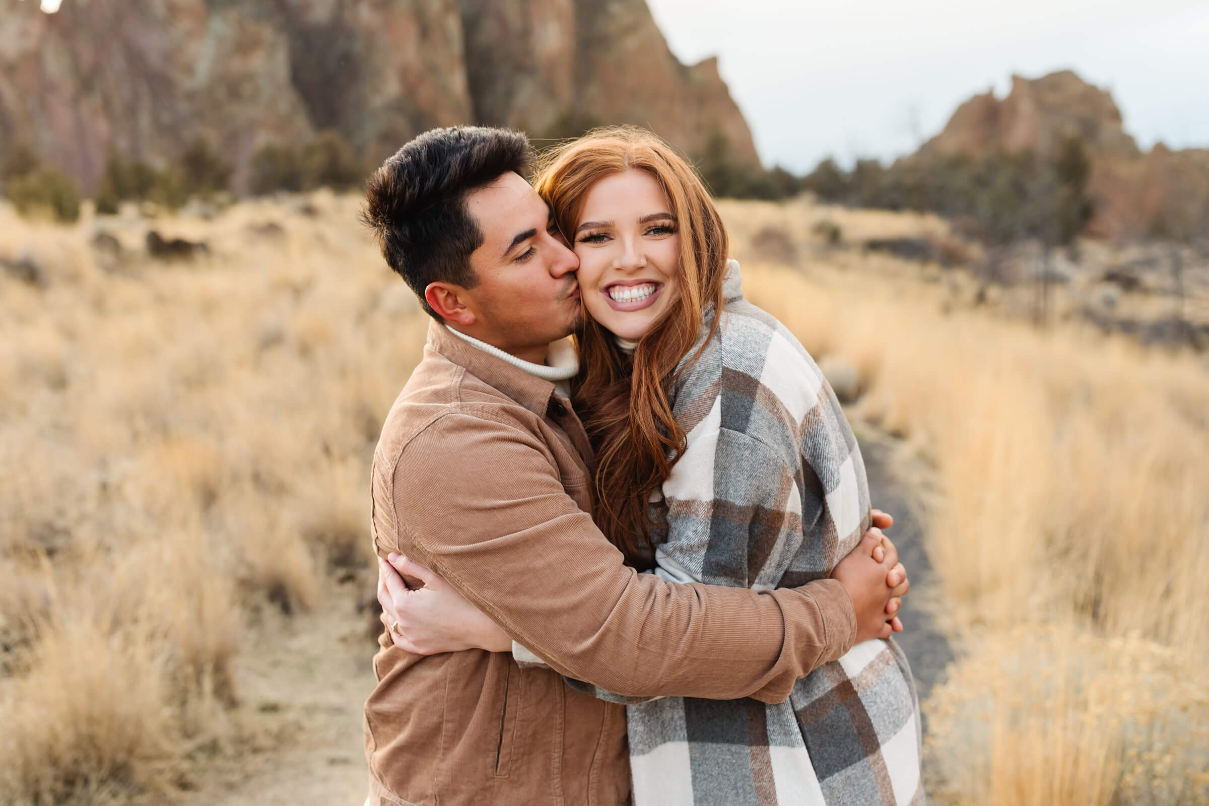 dark haired male in leather jacket kissing woman with red hair on the cheek during smith rock family photoshoot