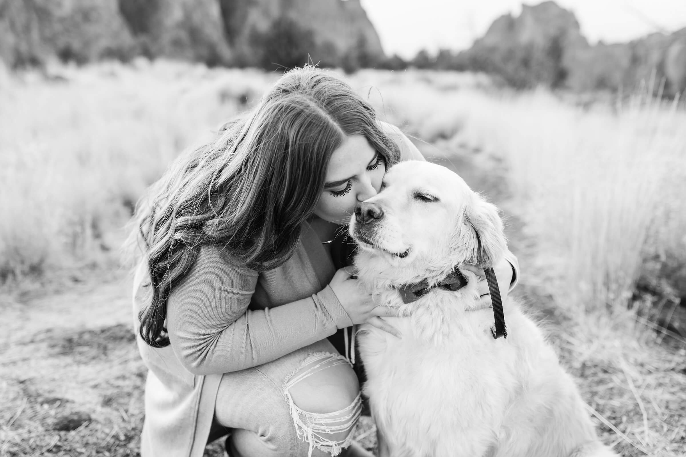 black and white image of woman kneeling and kissing golden retriever wearing bow tie at smith rock photoshoot