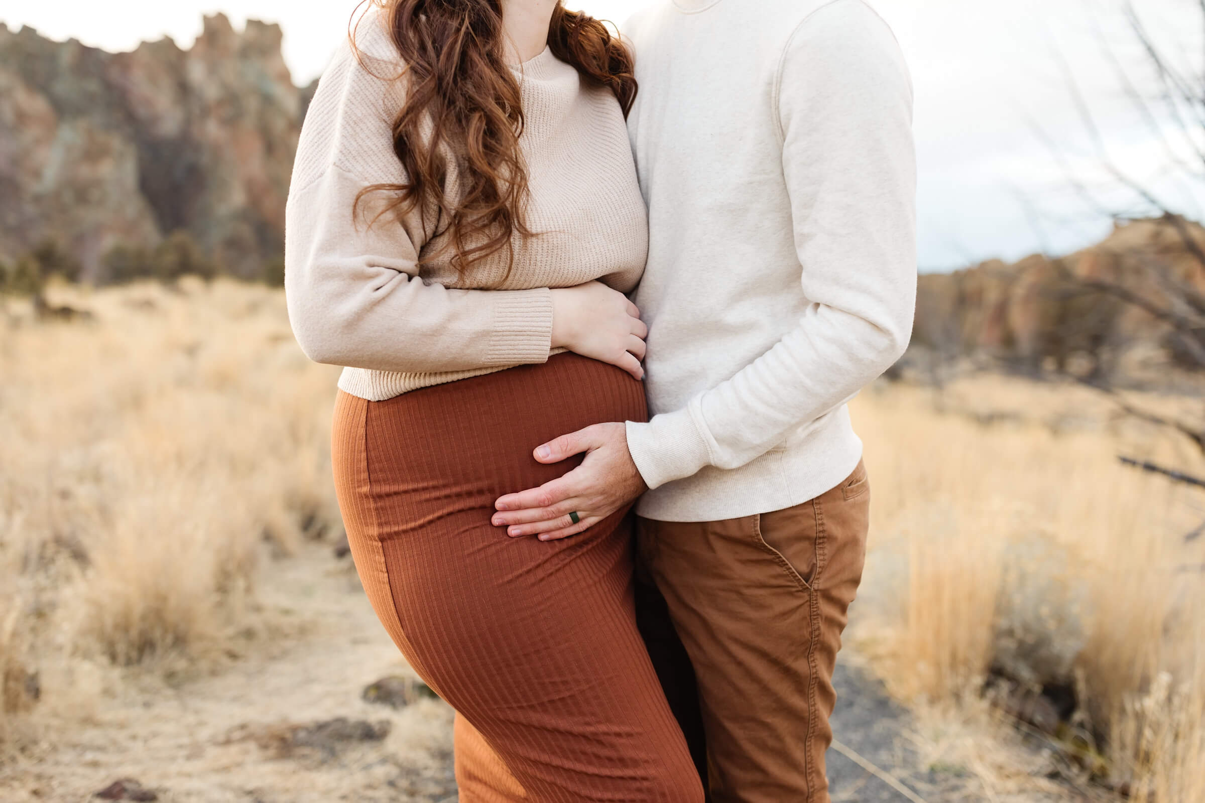 cropped image of pregnant belly in terracotta skirt with husband caressing her pregnant belly at smith rock