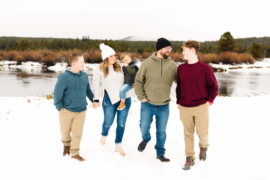 family of five holding hands and smiling at each other while walking through snow in Sunriver during family photoshoot