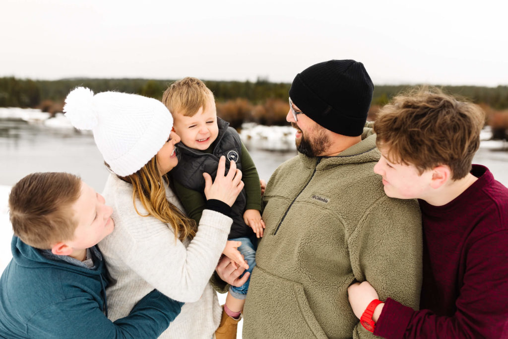 family of 5 cuddled together standing in the snow next to deschutes river during sunriver photoshoot